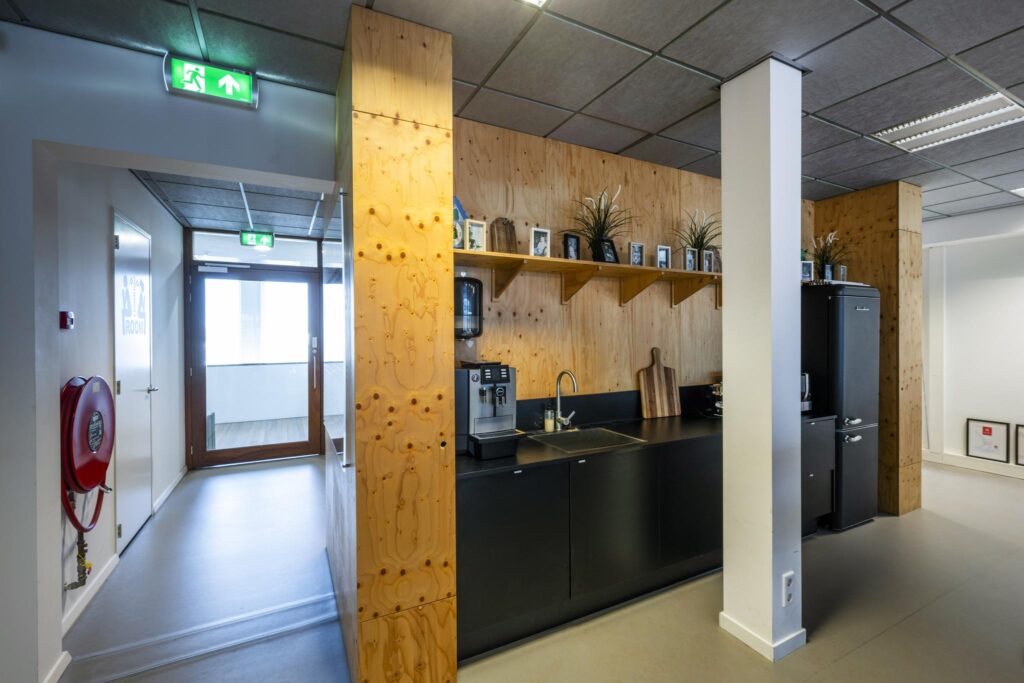 Moderne pantry in een kantoor aan de De Ruijterkade met zwarte keuken, koffieapparaat en houten wandafwerking.